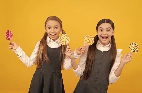 Niños felices en uniformes formales sostienen caramelos dulces dulces fondo amarillo, alegría —  Fotos de Stock