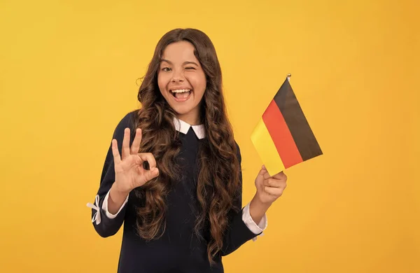 Feliz guiño niño mantenga bandera alemana fondo amarillo mostrando gesto ok, educación en el extranjero — Foto de Stock
