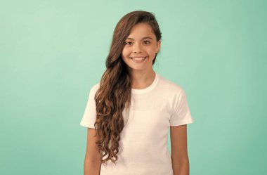 Neşeli çocuk, uzun kıvırcık saçlı, beyaz gömlekli mavi arka planda, saç bakımlı.