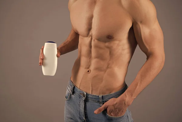 Man with six pack abs torso cropped view hold bottle of sport body wash grey background, bodywash — Stock Photo, Image