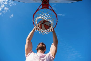 Oyuncu, basketbol topunu elle ve motivasyonla ağ çemberinde smaç basıyor.