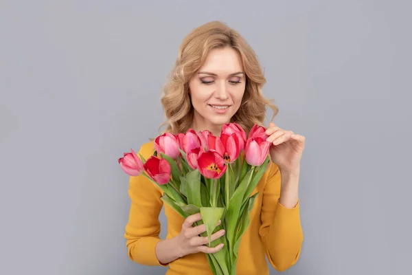 Pozitif bayan, bahar tatili için çiçekleri gri arka planda tutun. — Stok fotoğraf