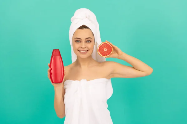 Vrolijk mooi vrouw in handdoek met grapefruit shampoo fles op blauwe achtergrond — Stockfoto