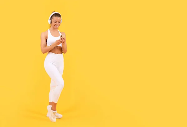 Mujer deportiva con auriculares y smartphone sobre fondo amarillo. espacio de copia —  Fotos de Stock