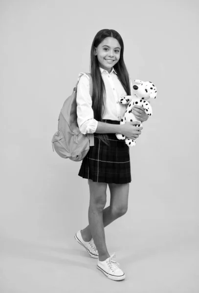 Wesoła nastolatka dziewczyna z plecakiem w mundurze szkolnym pełna długość na żółtym tle, czas szkolny. — Zdjęcie stockowe
