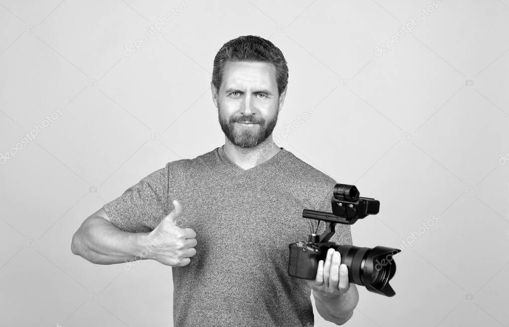cheerful bearded man videographer making movie for vlog with camcorder showing thumb up, filming