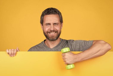 Sarı kağıdın arkasındaki mutlu sakallı adam spor salonu halterleri, reklam için.