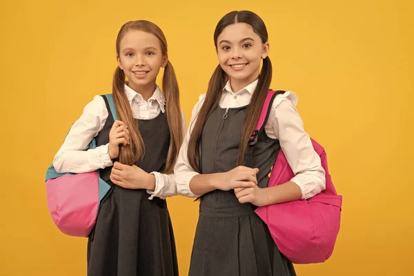 Glada barn bär skolväskor i formella mode uniformer gul bakgrund, tillbaka till skolan — Stockfoto