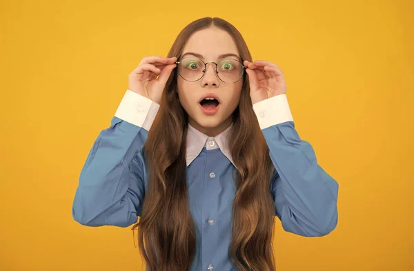 Chocado escola idade menina criança em óculos com olhar espantado amarelo fundo, espanto — Fotografia de Stock