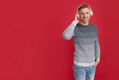 Sıradan giyinen, müzik kulaklığı takan, kırmızı arka planda müzik dinleyen mutlu bir adam.