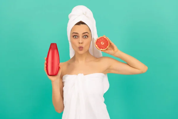 Verbaasd vrouw met grapefruit shampoo fles op blauwe achtergrond — Stockfoto