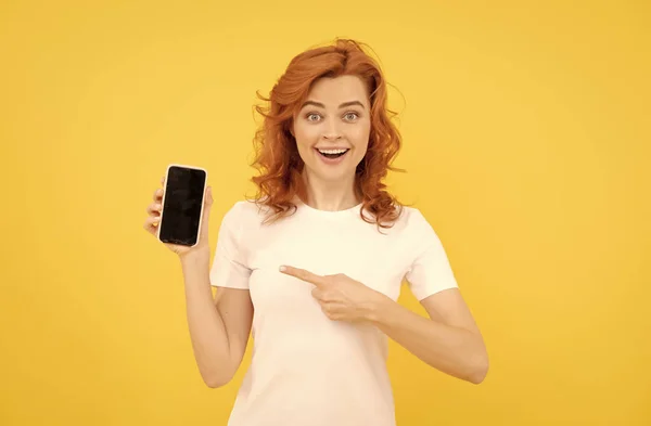 Excitada joven mujer aislado sobre fondo amarillo utilizando el teléfono móvil que muestra gesto ok. —  Fotos de Stock