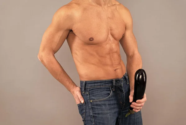 Muscular man cropped view hold firm and large eggplant at crotch level, penis enlargement.
