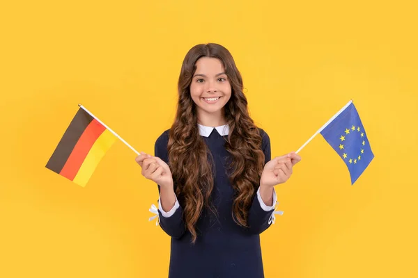 Χαμογελαστό παιδί κατέχει την Ευρωπαϊκή Ένωση και γερμανική σημαία κίτρινο φόντο, σπουδές στο εξωτερικό — Φωτογραφία Αρχείου