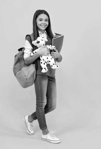 Feliz adolescente escuela chica con mochila y copybook celebrar juguete sobre fondo amarillo, lección —  Fotos de Stock