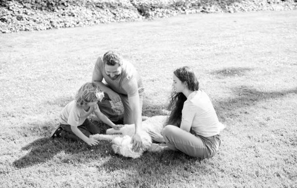 Día de la familia. amistad. padre madre e hijo en la hierba verde del parque. familia amigable con mascota. — Foto de Stock