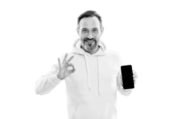 Heureux beau mature homme à capuche présentant smartphone écran copie espace isolé sur blanc, ok. — Photo