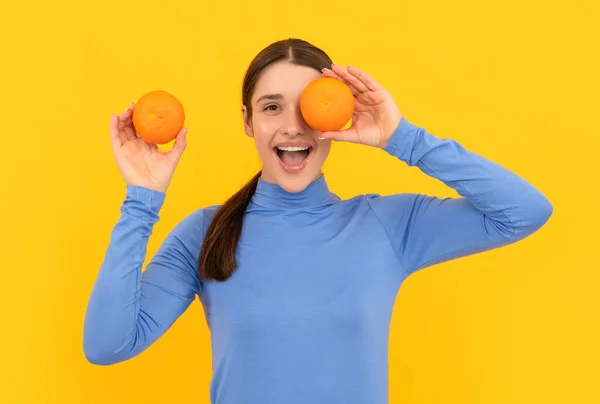 Espantado jovem mulher segurando laranja citrinos no fundo amarelo, saúde — Fotografia de Stock