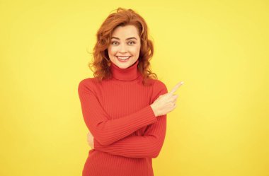 Sarı arka planda tek başına duran mutlu genç bayan. Kamera işaret ediyor.