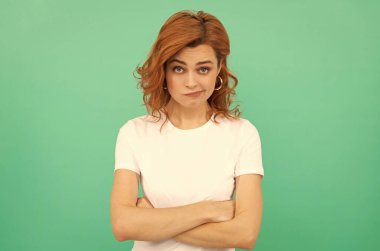 Mavi arka planda kıvırcık saçlı kafası karışık kızıl saçlı kadın ellerini çaprazladı, duygular içinde.