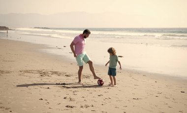 Mutlu baba-oğul futbol oynuyor. Yaz tatilinde eğleniyorlar. Kumsalda aile tatili, çocukluk.
