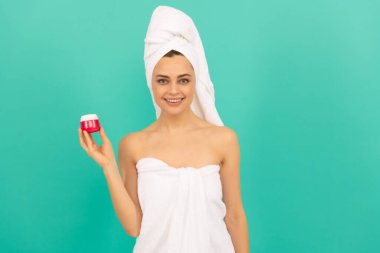 Mavi arka planda cilt kremi olan havlulu mutlu kadın.