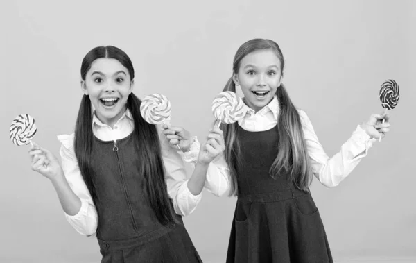 Niños felices en uniformes formales sostienen caramelos dulces dulces fondo amarillo, alegría —  Fotos de Stock