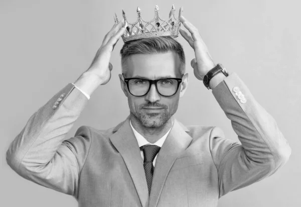 grizzled guy wearing king crown on grey background, success