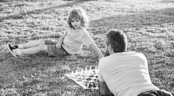 Szczęśliwa rodzina tatusia i synka grających w szachy na zielonej trawie w parku na świeżym powietrzu, rodzicielstwo — Zdjęcie stockowe