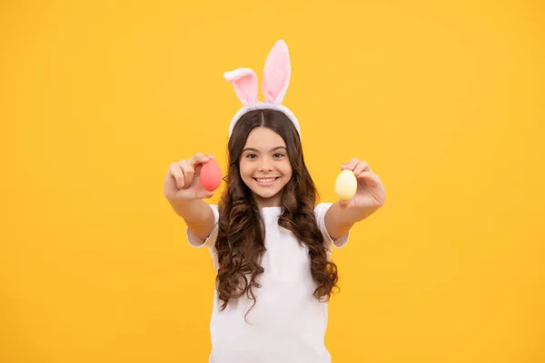 Il bambino allegro in orecchi di coniglio tiene uova su sfondo giallo, pasqua felice — Foto Stock