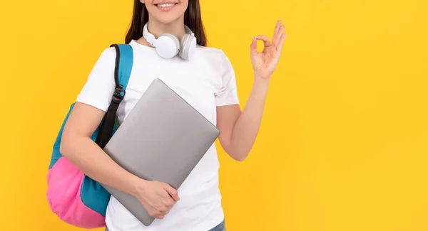 Mulher positiva com fones de ouvido e computador em fundo amarelo mostram gesto ok, e-learning — Fotografia de Stock