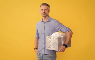 Gülümseyen adam hediye kutusunu sarı arka planda tut, alışveriş yap