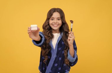 Rahat bornozlu mutlu kız pudra fırçasıyla tımar ediyor, ürünleri sunuyor.