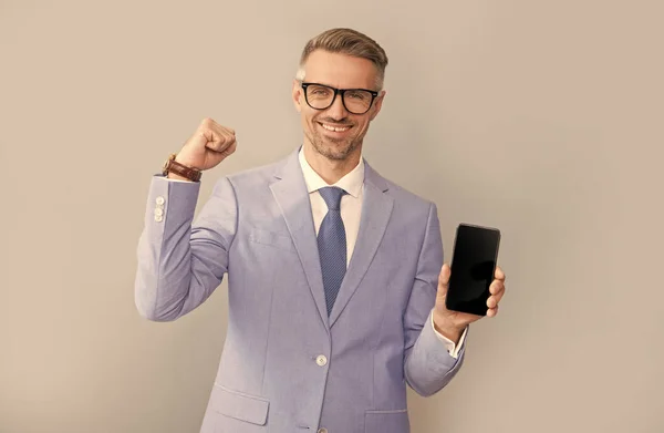 Glücklicher grimmiger Mann zeigt Handybildschirm in Anzug und Brille, neue App — Stockfoto