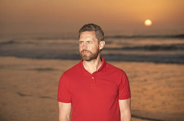 Barbudo bonito homem no verão camisa na praia com pôr do sol sobre o mar, relaxar — Fotografia de Stock