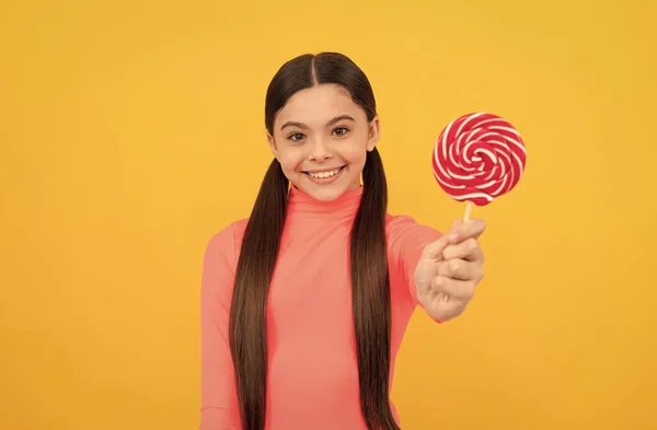 Gelukkig tiener meisje met lolly snoep op stok op gele achtergrond, candy shop — Stockfoto