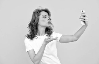 Kadın cep telefonuna el öpme hareketi yapıyor. Sarı arka plan, selfie.