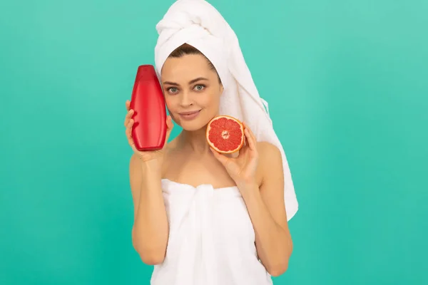 Vrolijk meisje in handdoek met grapefruit shampoo fles op blauwe achtergrond — Stockfoto