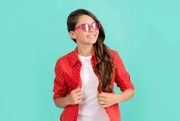 Lächelndes Kind mit langen lockigen Haaren posiert in Sonnenbrille und lässigem Hemd, modischer Stil — Stockfoto