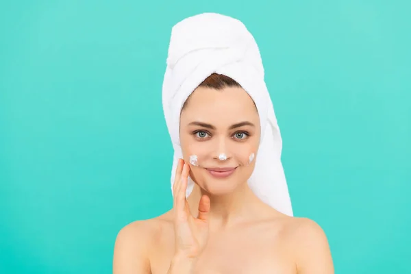 Usmívající se mladá dáma použít krém na obličej na modrém pozadí — Stock fotografie