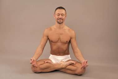 Yogi adam, Lotus Yoga pozisyonunda oturup meditasyon yapıyor. Gri arka plan, meditasyon.