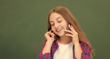 Mutlu çocuk akıllı telefondan konuşuyor. Sınıfta, tahtada, kopyalama alanında, konuşmada.