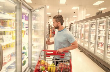 Alışveriş arabalı bir adam marketten yemek alıyor, tüketiyor.