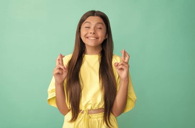 Mutlu genç kız ellerini çapraz yapıp mavi arka planda şans diliyor.