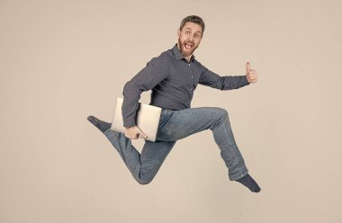 Enerjik patron bilgisayarı tutuyor. Baş parmak hareketi. Bilgisayarda çalışan zıplayan iş adamı.