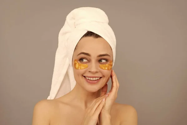 Felice ragazza con asciugamano di spugna uso viso patch occhi dorati per la pelle, pelle sana — Foto Stock