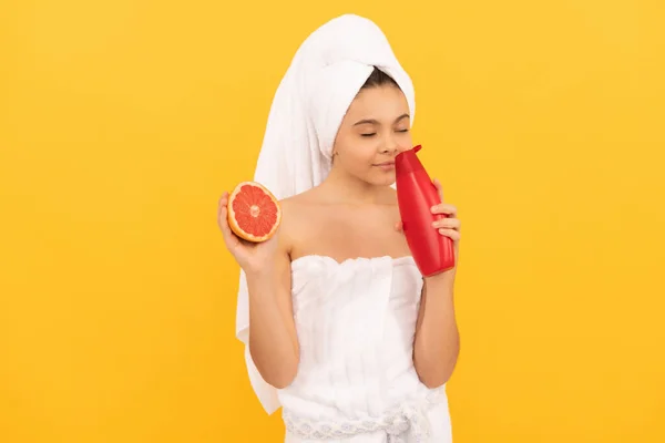 Happy child in towel smell grapefruit shampoo bottle on yellow background — Stock Photo, Image