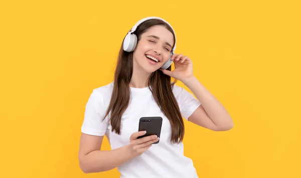 Young girl listen music in headphones hold phone on yellow background, gadget — Stock Photo, Image