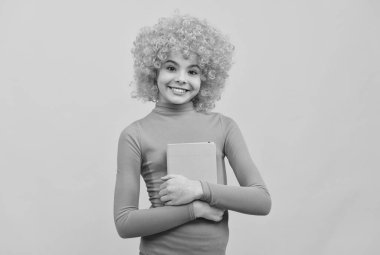 Pembe polonezli turuncu saçlı mutlu bir kız çocuğu. Elinde kitap sarısı arka plan, okul.