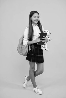 Sırt çantası oyuncağı ve okul üniformalı neşeli çocuk. Sarı arka planda uzun boylu, çalışkan.